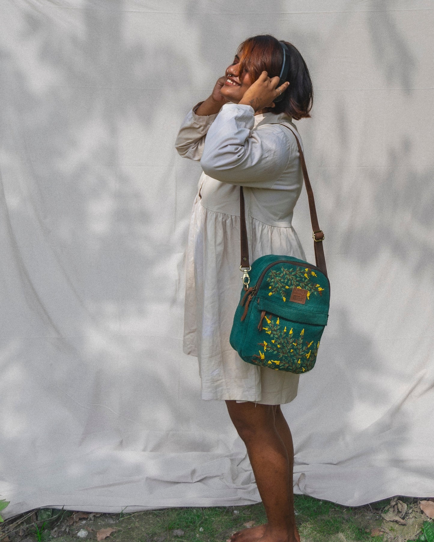 Woman holding a teal backpack with floral patterns against a white curtain background