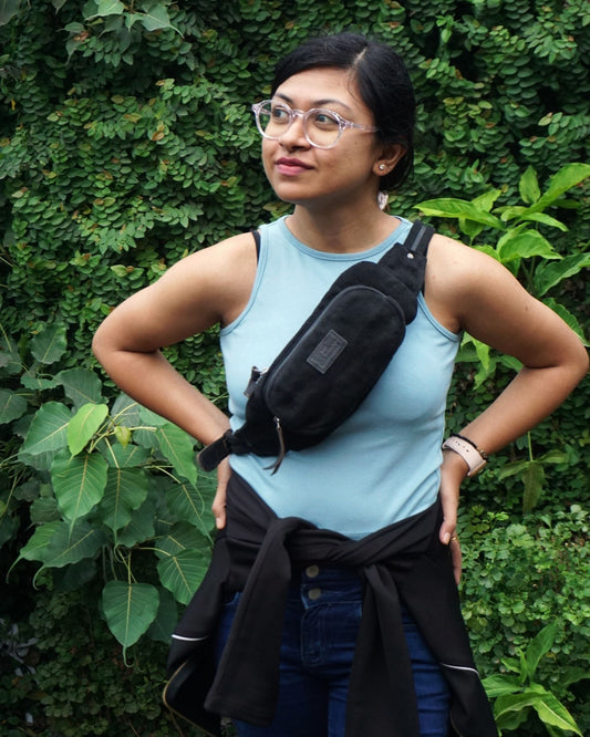 Black handcrafted burlap fanny pack by The Burlap People worn crossbody against green foliage