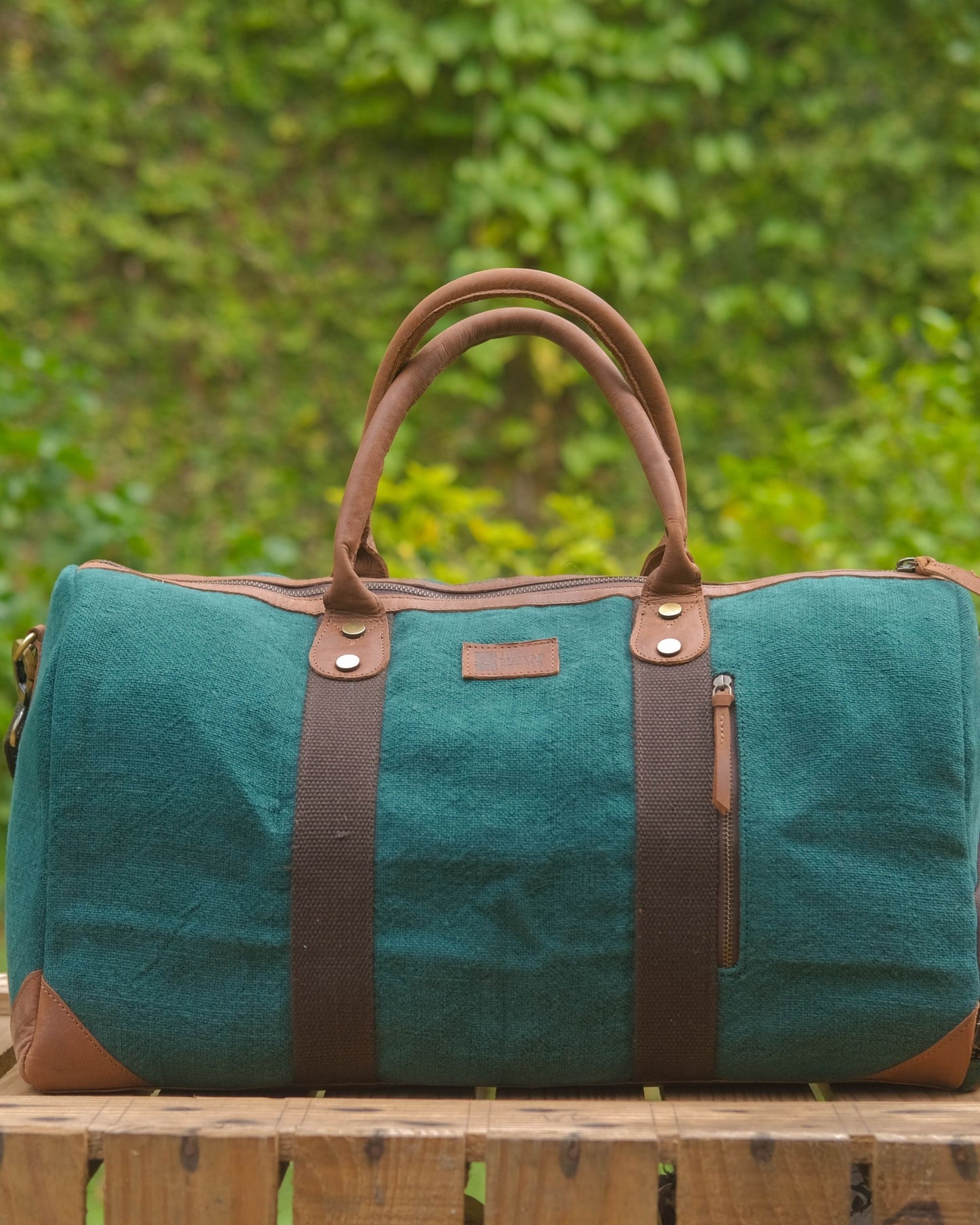 Bottle Green Duffel 2.0 mini front view showing vintage suede like texture, top leather handles, vertical zipper pocket and leather accents. 