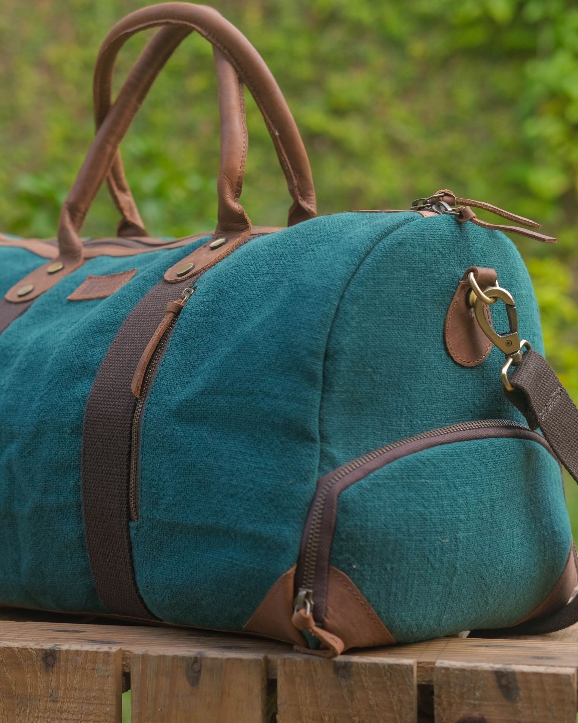 Mini Duffel 2.0 in Bottle Green burlap side view showing external shoe compartment zip leather reinforced corners brown web tape contrast side zip pocket leather patch brass dog hook shoulder strap attachment and tan leather top handles with brass zipper