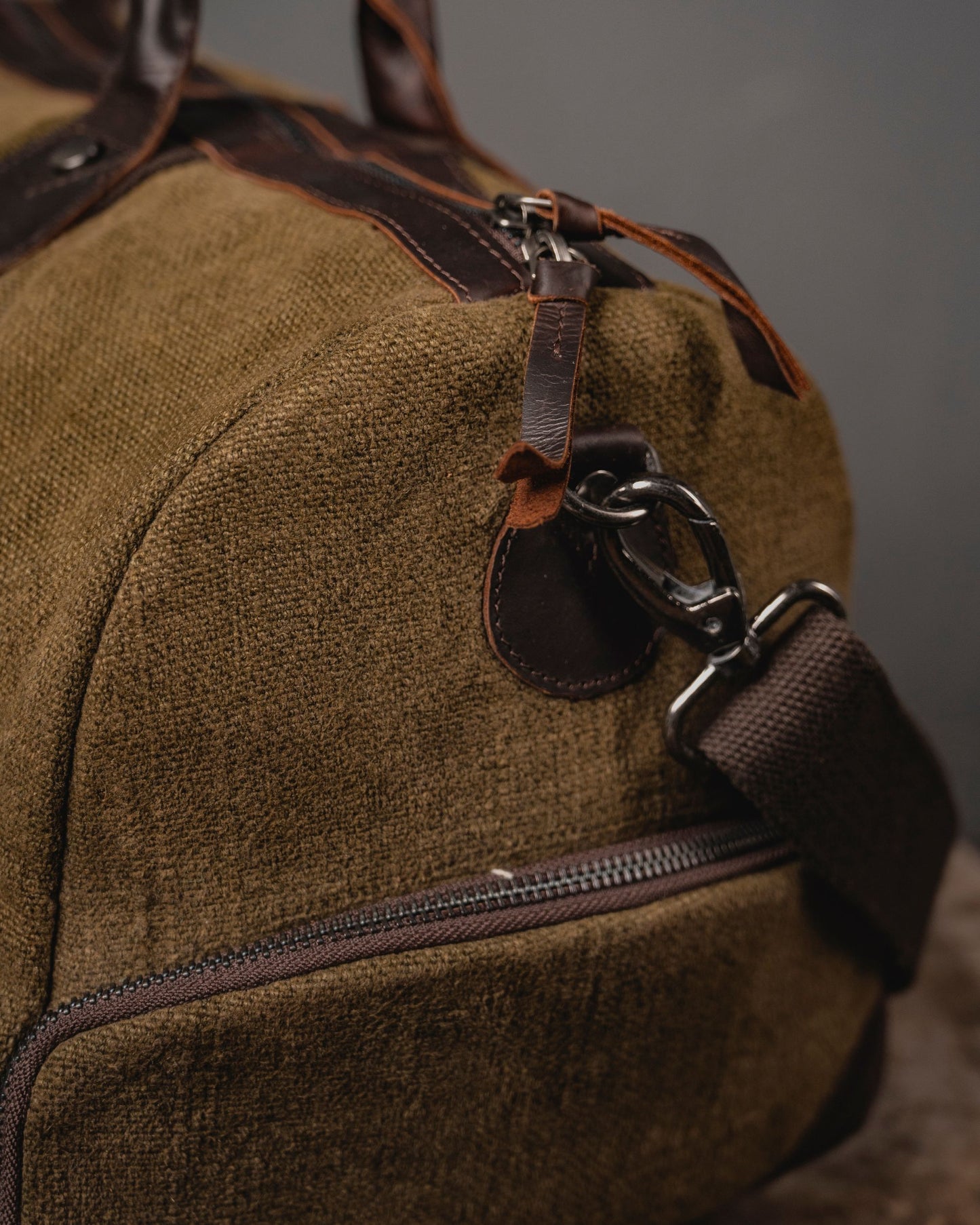 Close-up of antique brass dog hook and leather strap attachment on Brown Mini Duffel 2.0 showing 660 GSM burlap canvas texture and YKK zipper.