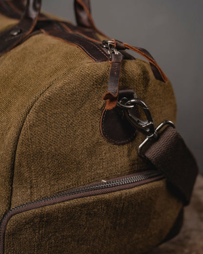 Close-up of antique brass dog hook and leather strap attachment on Brown Mini Duffel 2.0 showing 660 GSM burlap canvas texture and YKK zipper.