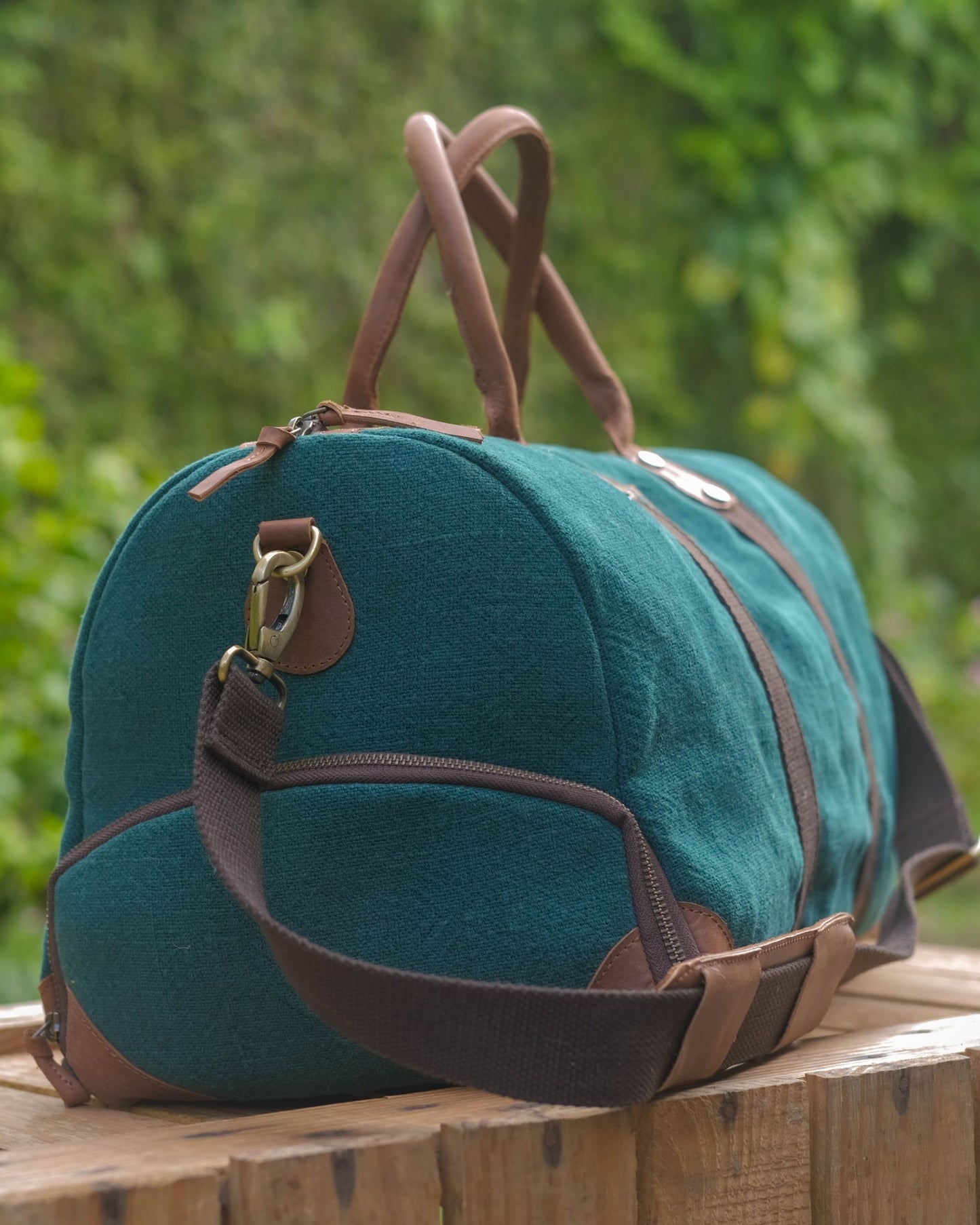 Mini Duffel 2.0 in Bottle Green burlap side view showing external shoe compartment zip leather patch with brass dog hook shoulder strap attachment padded leather shoulder strap and tan leather top handles