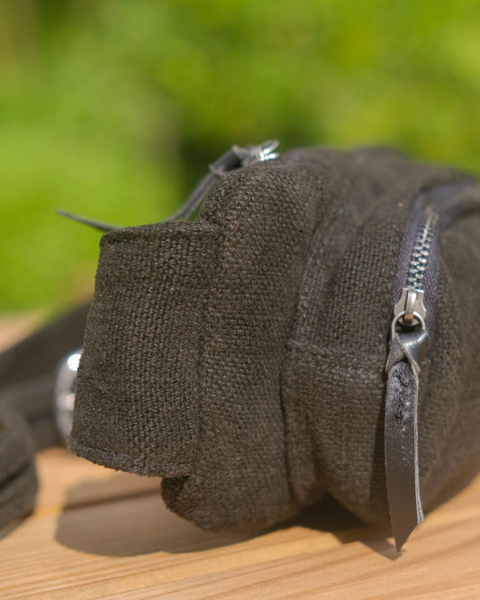 Close up of a black burlap fanny pack on a wooden crate showing zipper detail leather puller and natural woven texture
